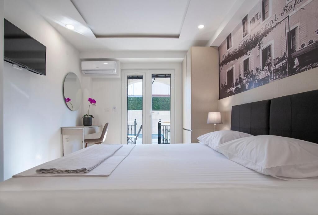 A bedroom with a bed, a desk, a chair, a TV, and a balcony with a view.