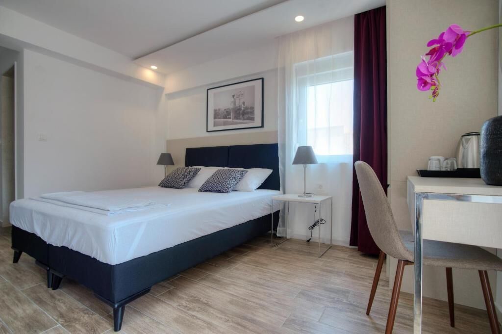 Habitación de hotel con cama, mesita de noche, silla, escritorio y ventana con cortinas.