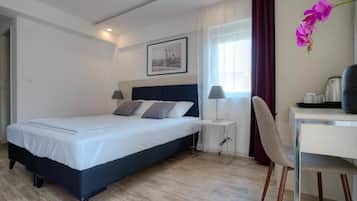 Habitación de hotel con cama, mesita de noche, silla, escritorio y ventana con cortinas.