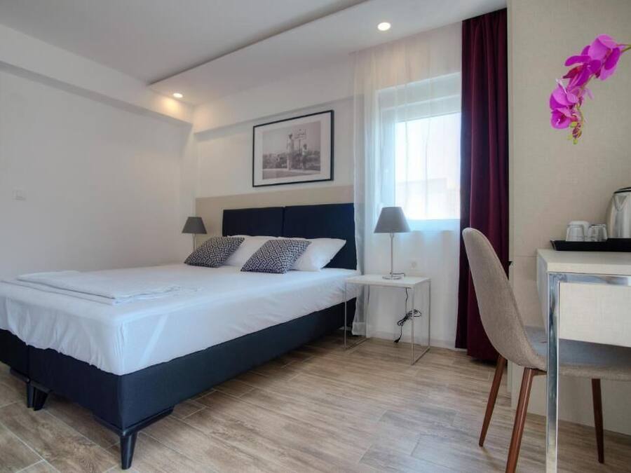 Habitación de hotel con cama, mesita de noche, silla, escritorio y ventana con cortinas.