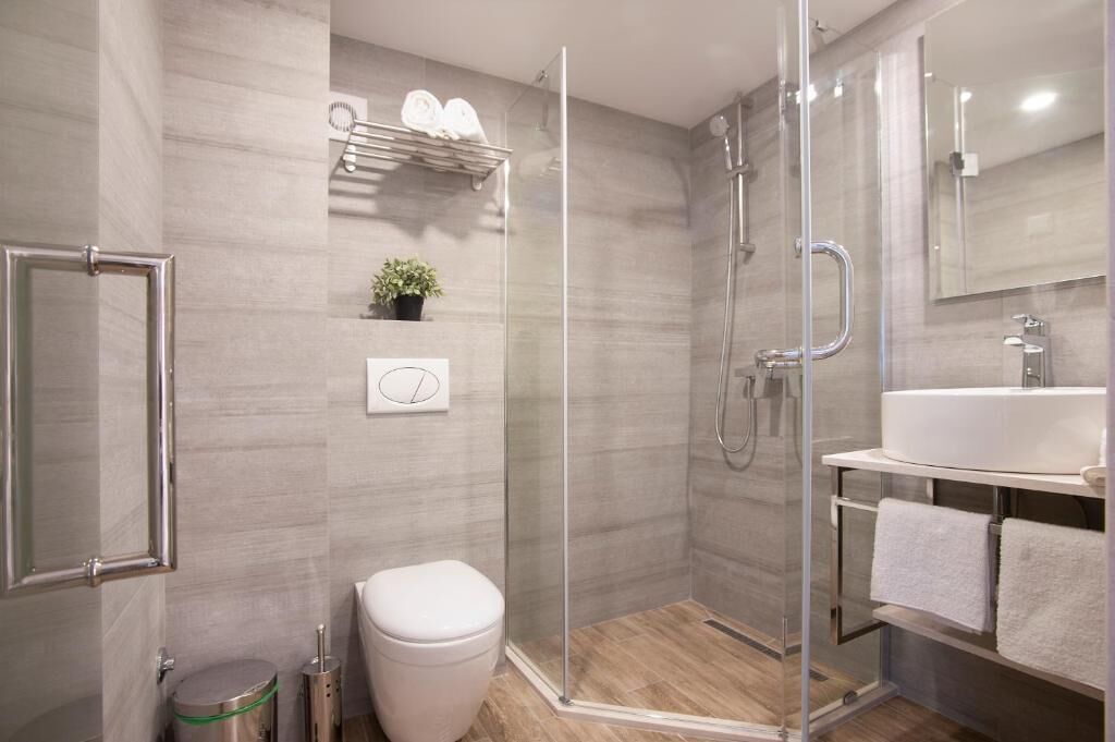 A modern bathroom with a glass shower enclosure, a toilet, a sink with a mirror, and a towel rack.