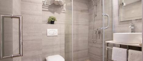 A modern bathroom with a glass shower enclosure, a toilet, a sink with a mirror, and a towel rack.