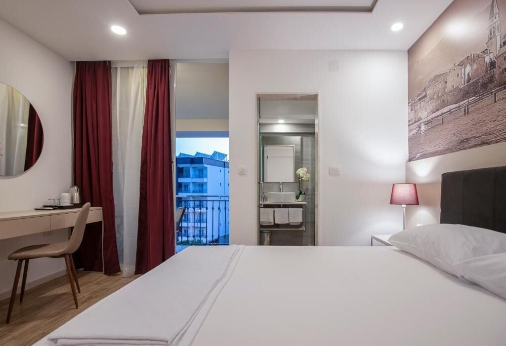 Habitación de hotel con cama, escritorio, silla, baño y balcón con vistas.