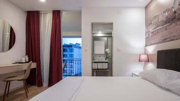 Habitación de hotel con cama, escritorio, silla, baño y balcón con vistas.