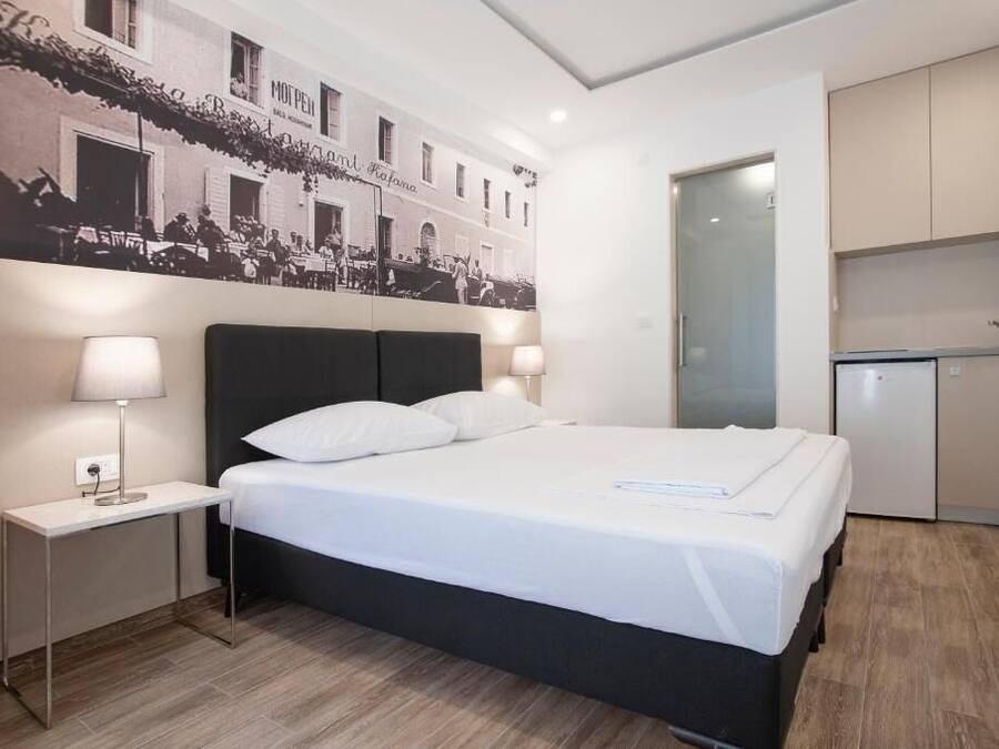 Una habitación de hotel moderna con cama, lámparas de noche, un pequeño escritorio y una kitchenette.