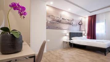 Ein Hotelzimmer mit einem Bett, einem Schreibtisch mit Blumen, einem Stuhl, einem Nachttisch mit einer Lampe und einer Wand mit einem Stadtbild.