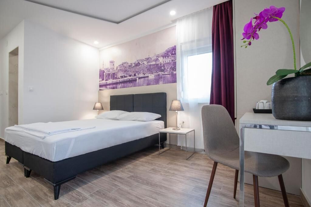 Una habitación de hotel con cama, mesitas de noche, escritorio, una silla y una orquídea morada.