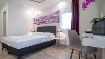 Una habitación de hotel con cama, mesitas de noche, escritorio, una silla y una orquídea morada.