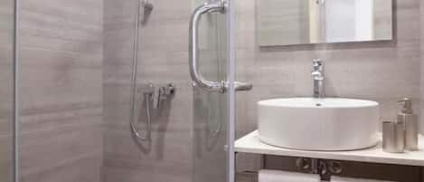 Un baño moderno con ducha de vidrio, lavamanos blanco y espejo superior.
