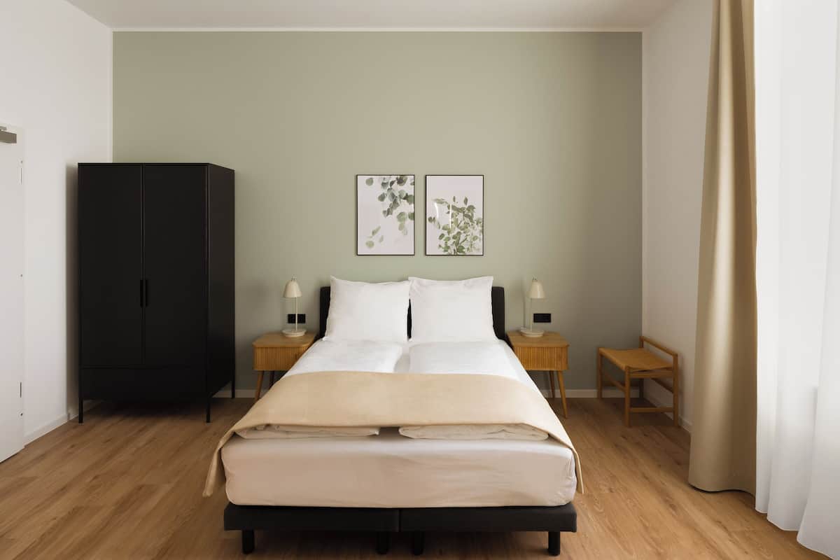 Un dormitorio con cama, dos mesitas de noche, un armario y dos cuadros en la pared.