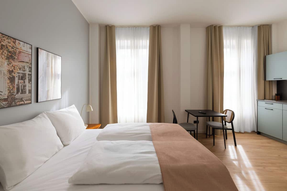 Una habitación de hotel con cama, escritorio, silla y kitchenette.