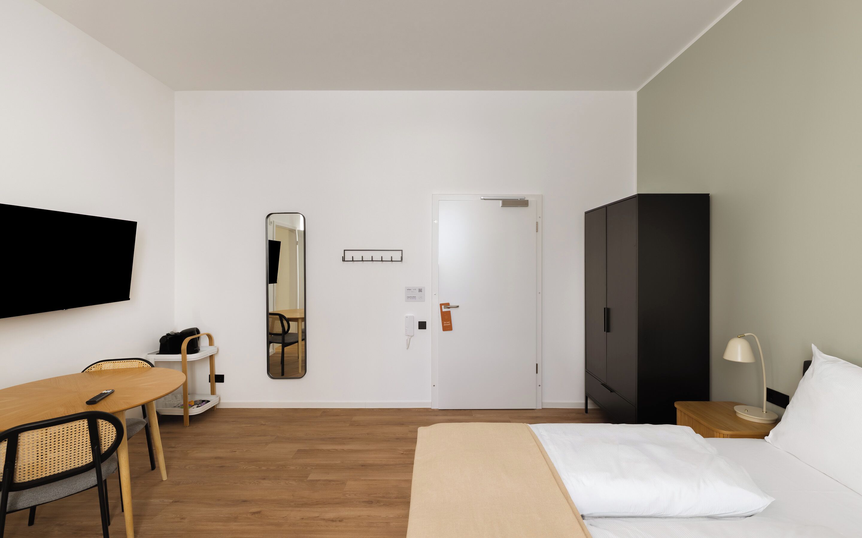 A hotel room with a bed, a desk, a chair, a television, a wardrobe, and a mirror.