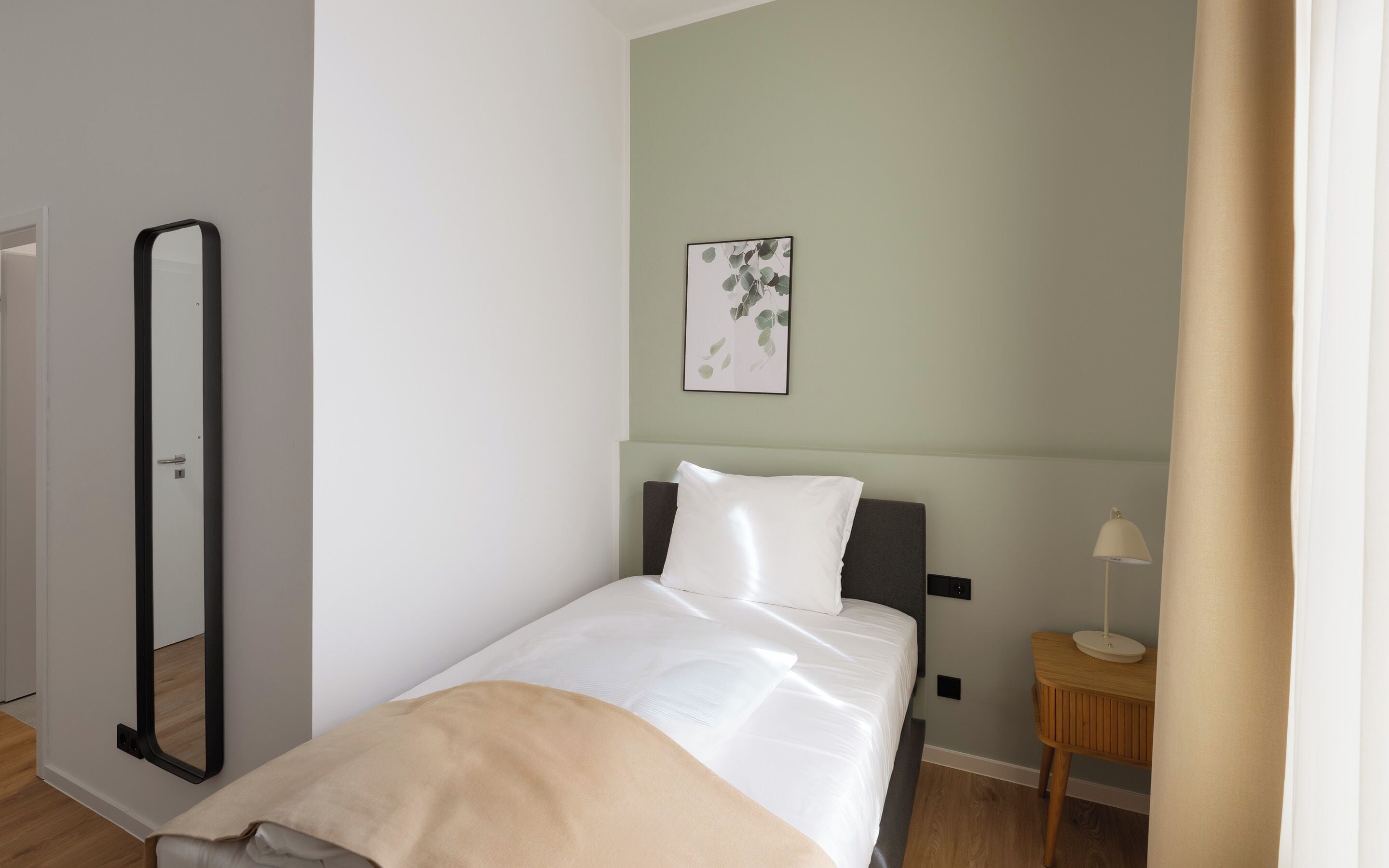 Un dormitorio con cama, una mesita de noche con lámpara, un cuadro en la pared y una puerta.