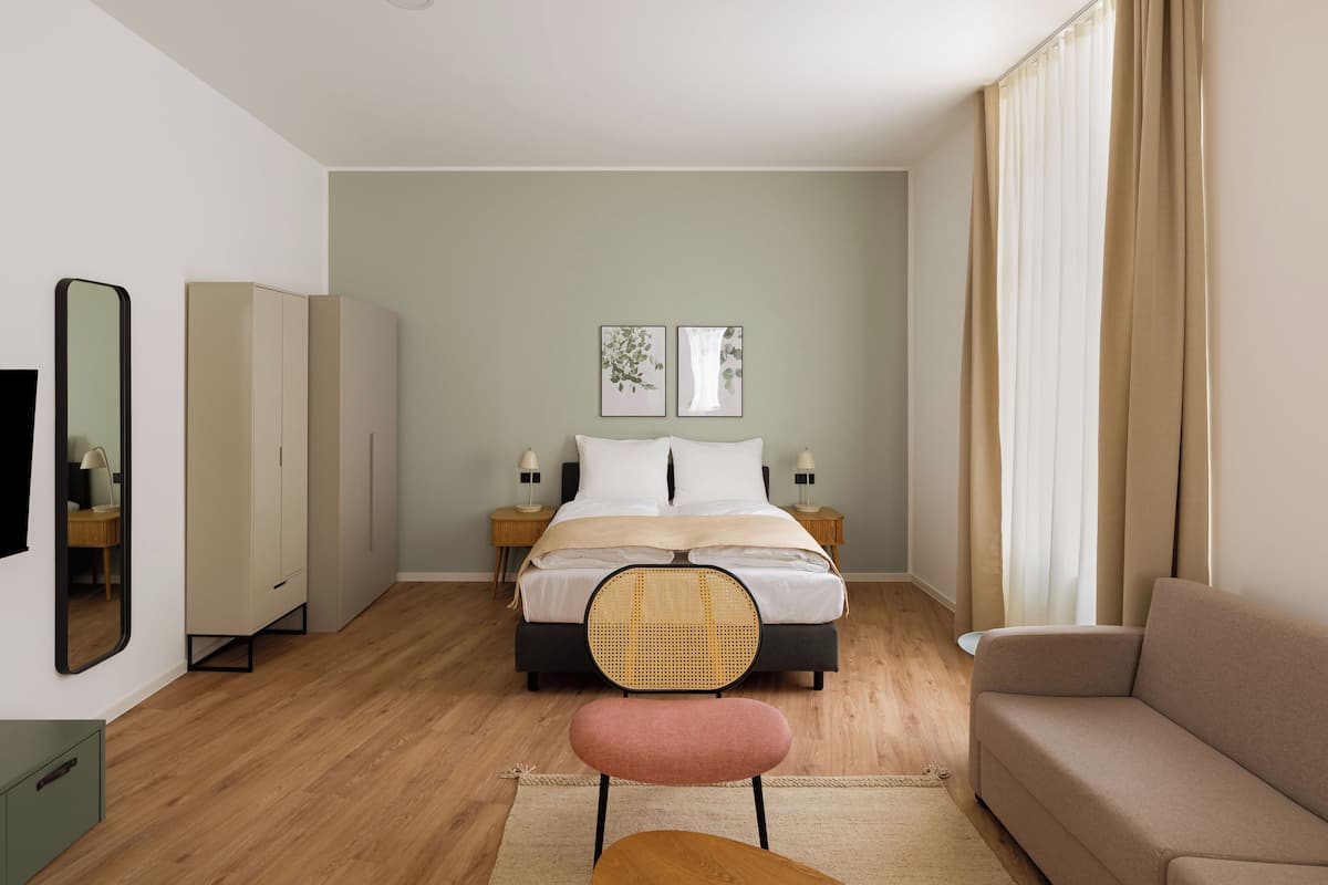 Un dormitorio con cama, mesitas de noche, una silla, un sofá, un espejo y obras de arte en la pared.