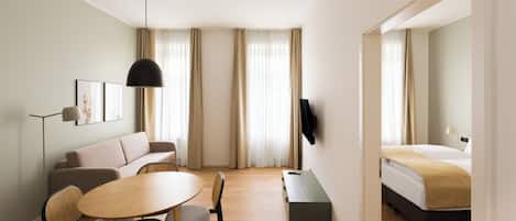 Ein modernes Hotelzimmer mit einer Couch, einem Esstisch mit Stühlen, einem an der Wand befestigten Fernseher und einem Bett.