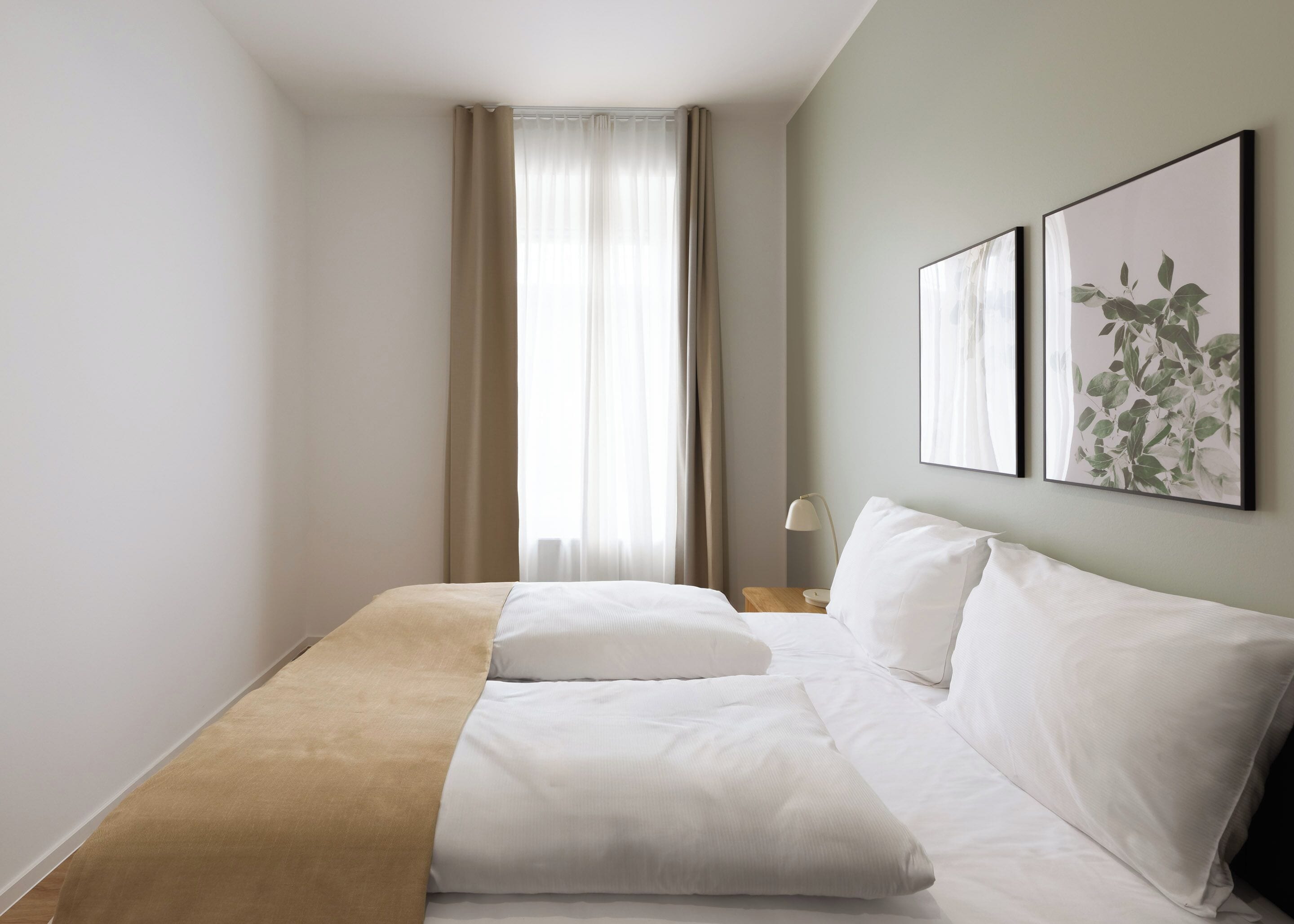 A hotel room with a bed, a nightstand, a lamp, and two framed pictures on the wall.