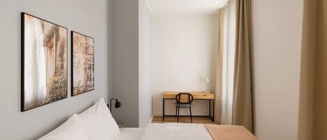A hotel room with a bed, a desk, a chair, and two framed pictures on the wall.