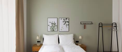 A neatly made bed with white linens, two bedside tables with lamps, and two framed botanical prints on the wall.