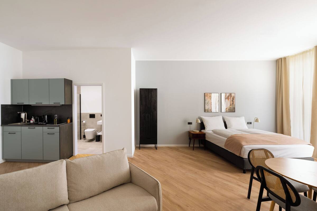 Una habitación de hotel moderna con kitchenette, cama, sofá y zona de comedor.