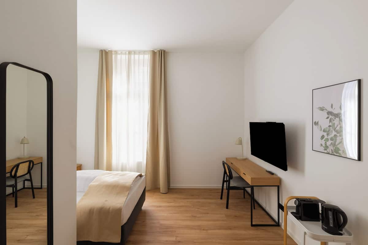 Habitación de hotel con cama, escritorio con televisor, silla, cafetera y un espejo grande.