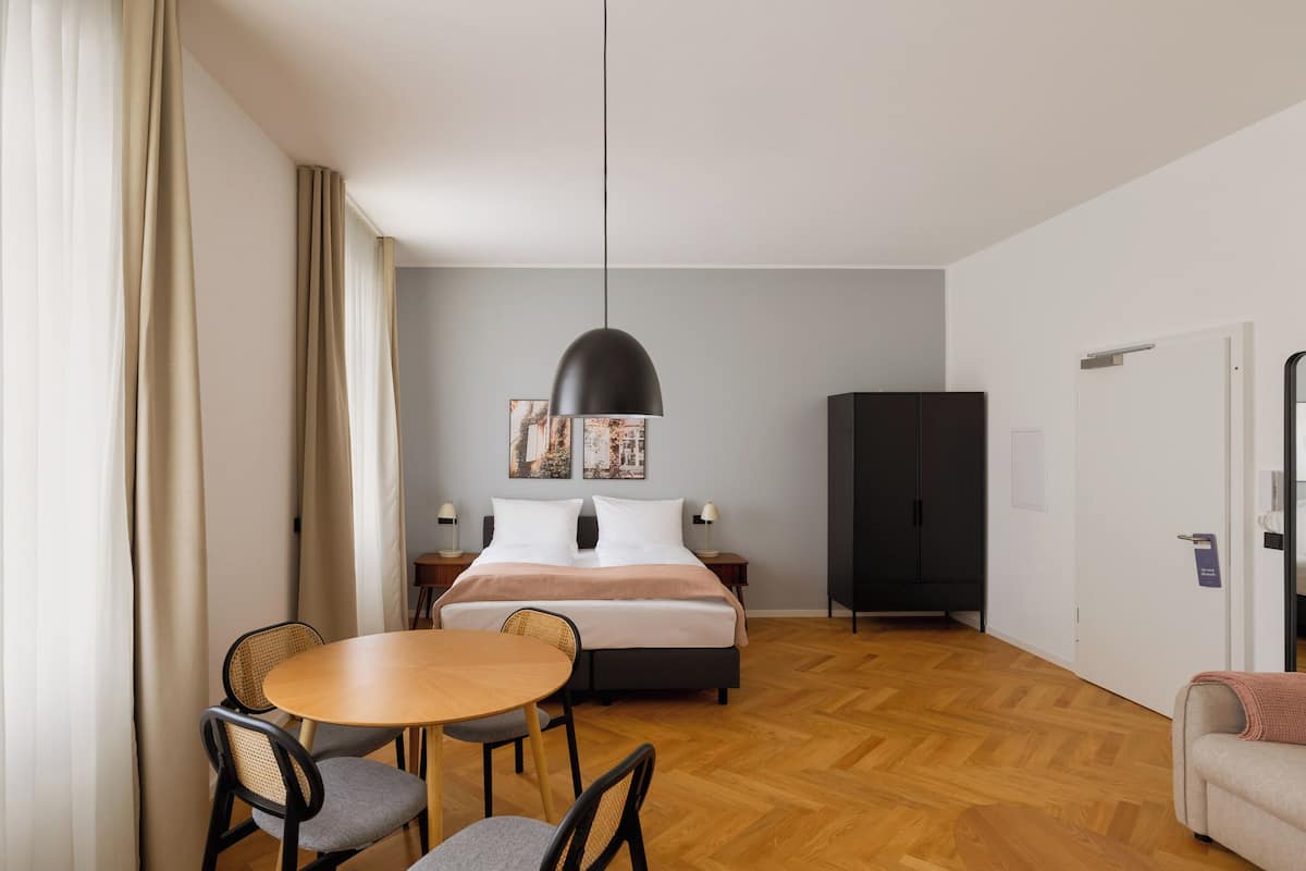 Una habitación de hotel con una cama, una mesa con sillas, un armario y una puerta.
