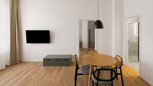 Uma sala de estar moderna com uma TV de tela plana, uma mesa de jantar com cadeiras, um banco e um lustre.