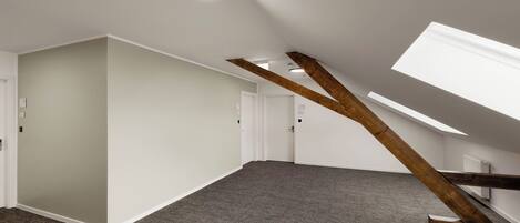 A spacious room with a sloped ceiling, exposed wooden beams, and a carpeted floor.