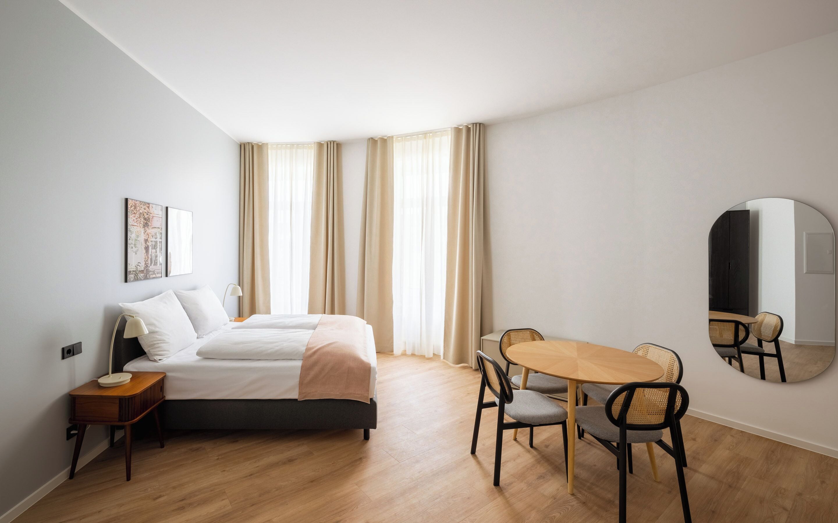 Een hotelkamer met een bed, nachtkastje, lamp en een ronde spiegel aan de muur.