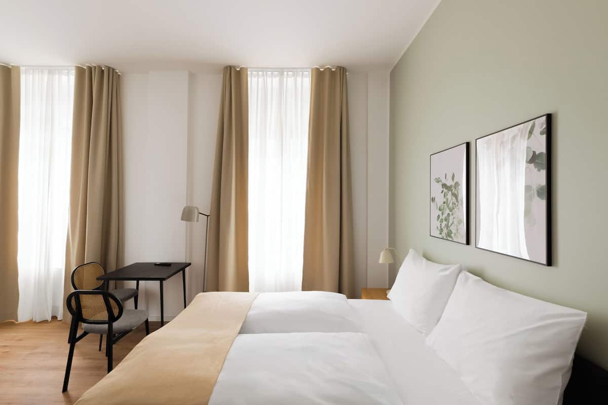 Una habitación de hotel con una cama, un escritorio, una silla y dos cuadros en la pared.
