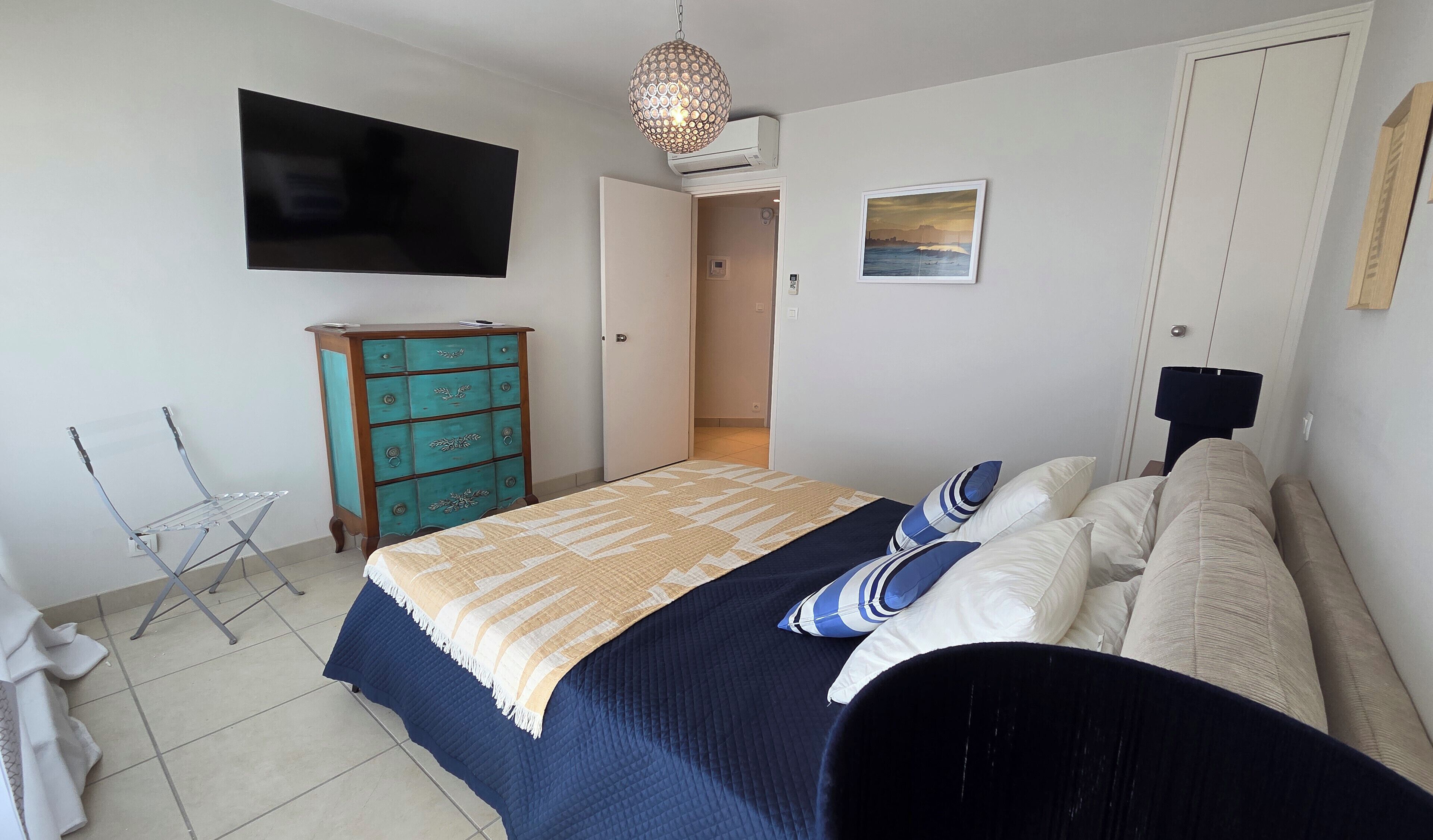 Ein Schlafzimmer mit einem Bett, einem Schminktisch, einem Fernseher und einer Tür zu einem weiteren Raum.