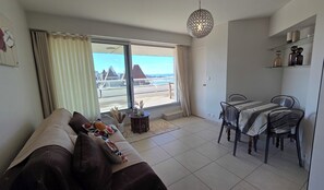 A living room with a sofa, a dining table with chairs, a decorative lamp, and a view of the sea through a large window. - Panoramic view and terrace in Biarritz (Biarritz)