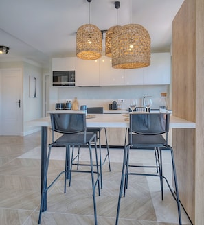 A modern kitchen with two hanging wicker chandeliers, a white countertop, and black chairs. - Panoramic sea view in Cannes (Cannes)
