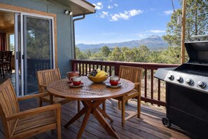 Um terraço com uma mesa posta para dois, churrasqueira e vista panorâmica das montanhas.