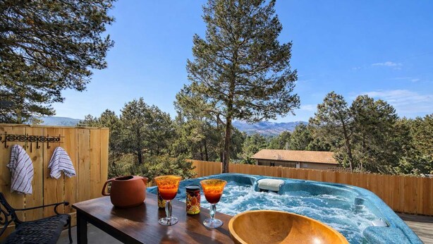 Une terrasse en bois avec un jacuzzi, un grand saladier en bois et une table avec des boissons et une plante en pot.