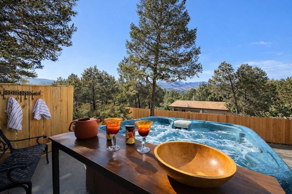 A wooden deck with a hot tub, a wooden bowl, and a table with drinks and a pot.