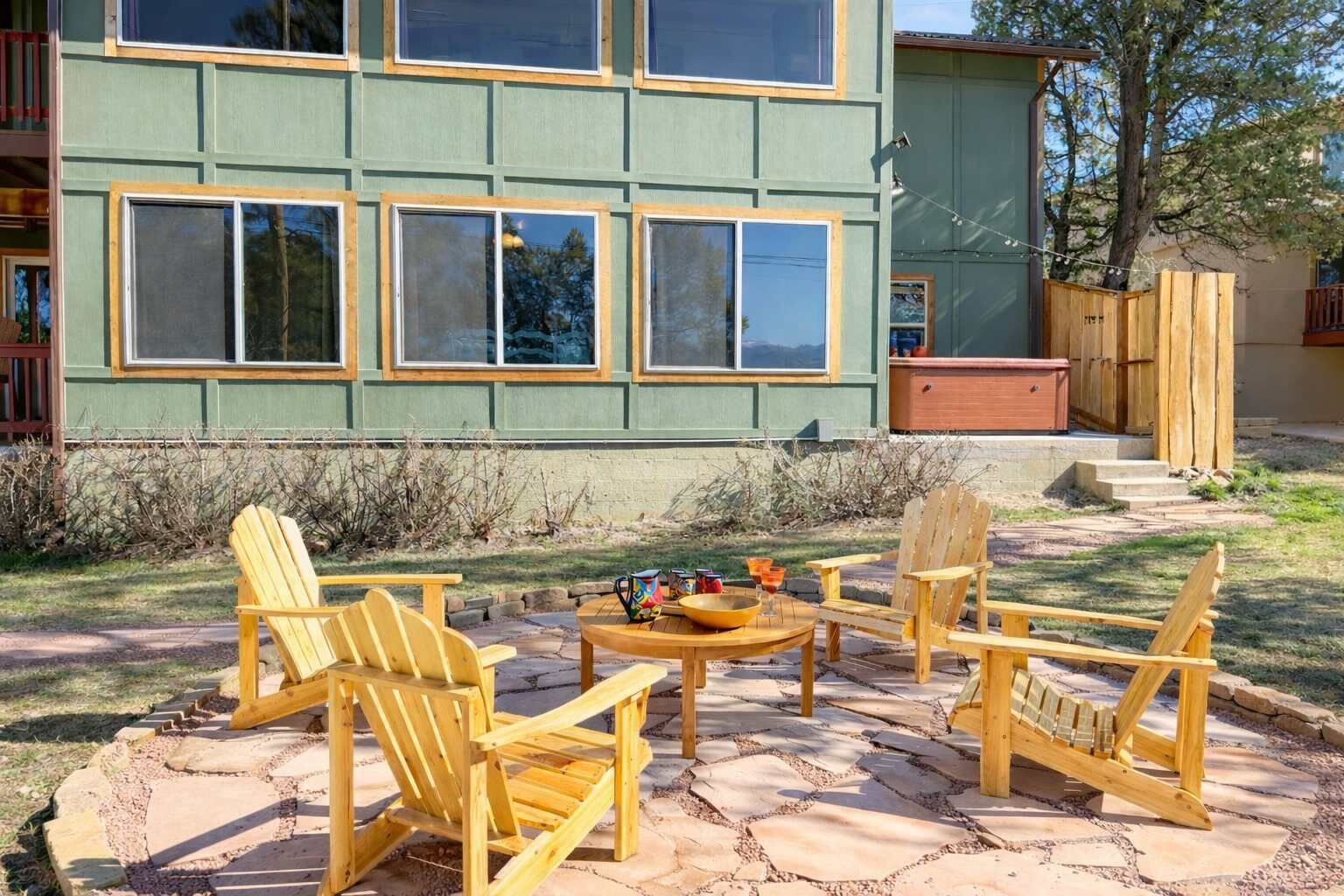 A building with large windows, a patio with wooden chairs and a table, and a small deck area.