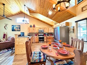 A cozy kitchen with wooden cabinets, a refrigerator, and a dining table set for four. - Casa La Luz  An Elegant Mountain Retreat (Ruidoso)