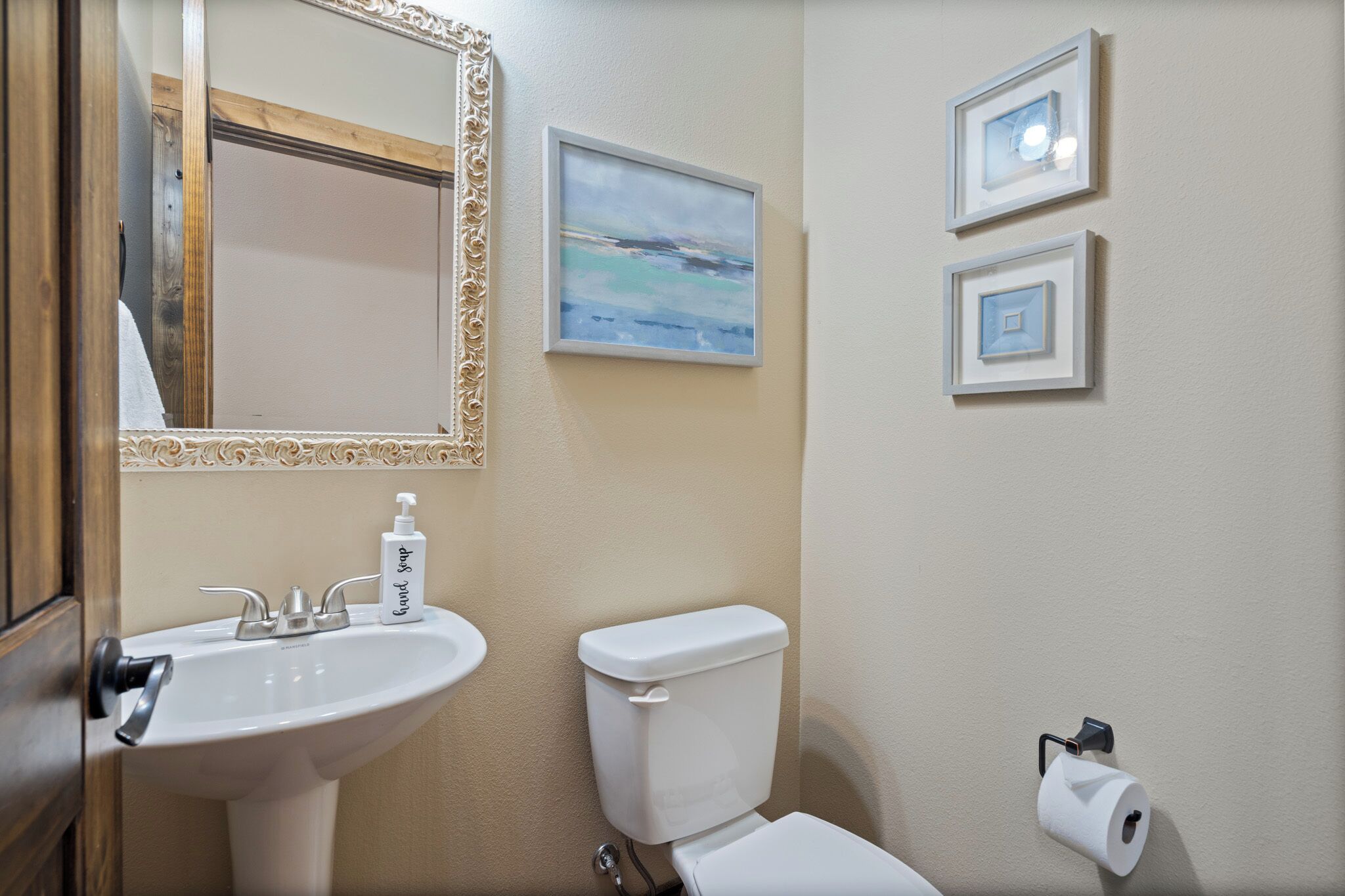 A bathroom with a sink, toilet, and framed artwork on the wall.