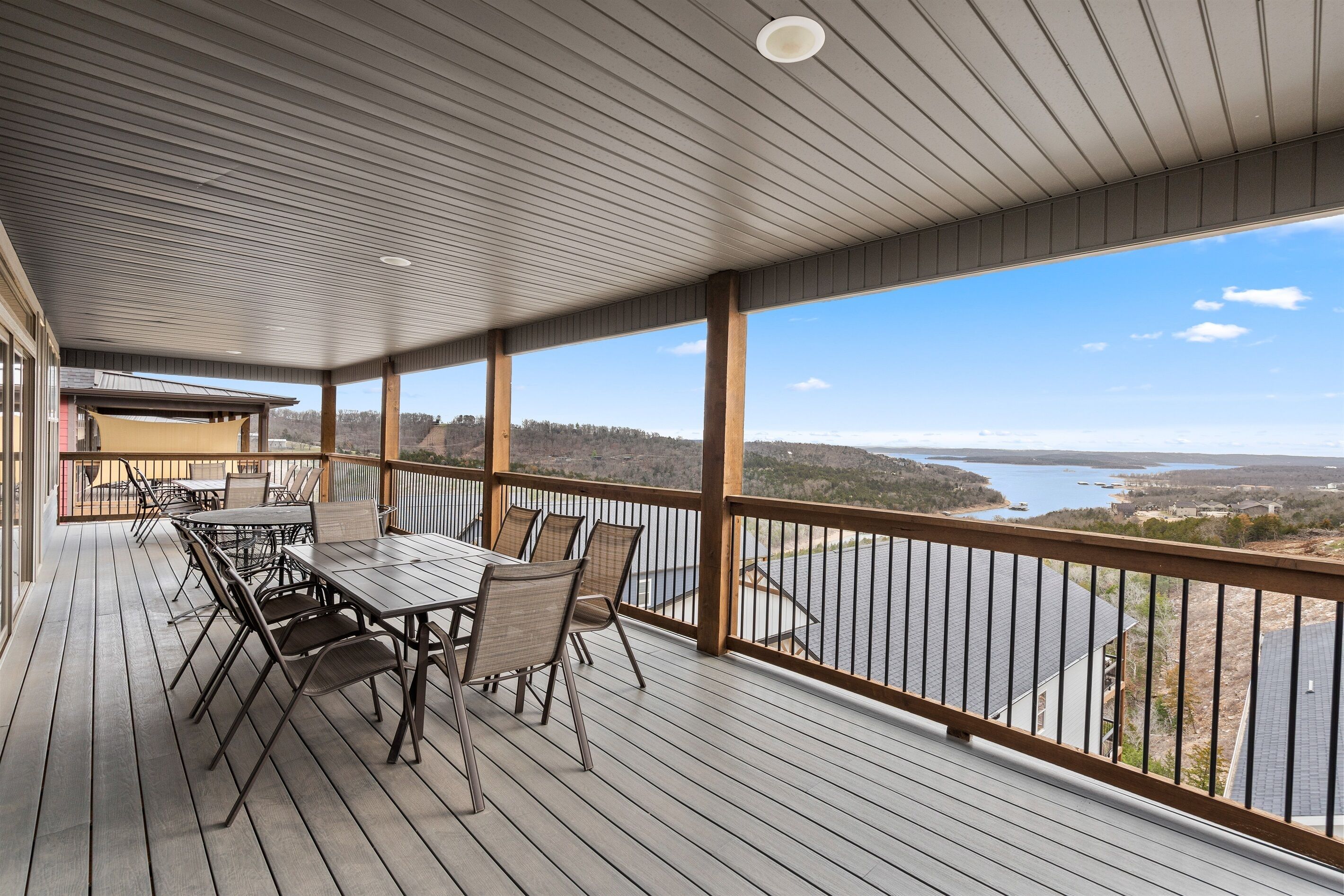 A covered outdoor deck with a table and chairs, overlooking a body of water and distant land.