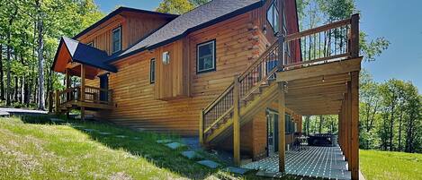 A wooden cabin with a deck and stairs leading to a covered area.
