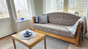 A cozy room with a patterned sofa, a small wooden table with a candle, and a view through large windows.