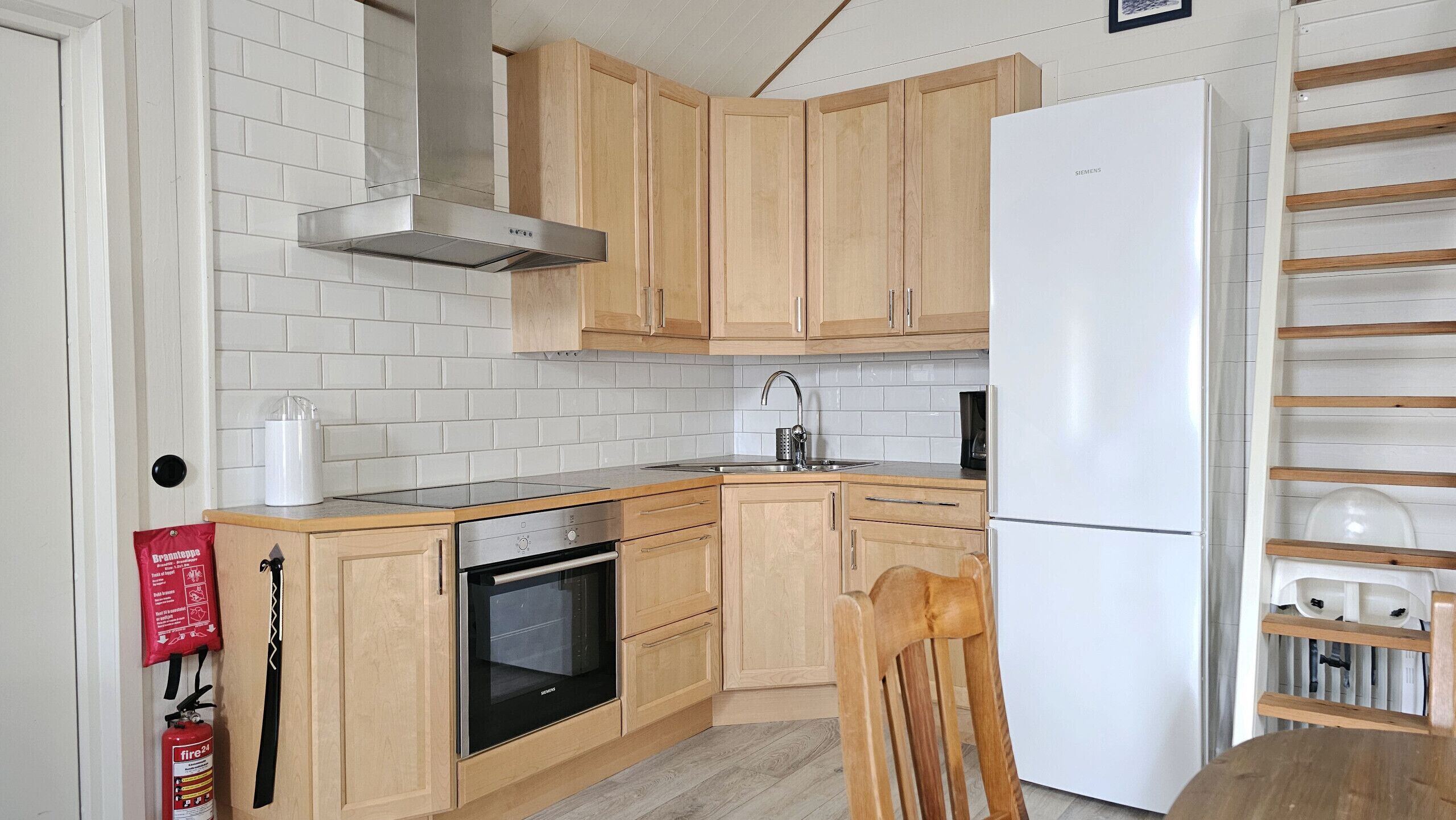 Una cucina con mobili in legno, una cappa in acciaio inossidabile, forno integrato, lavello e frigorifero bianco.
