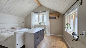 Quarto com cama, cômoda, janelas e teto inclinado.