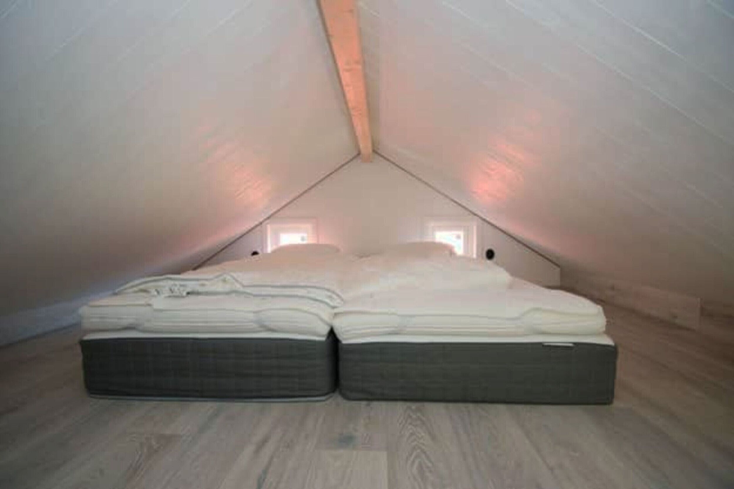 Un dormitorio ático pequeño y triangular con una cama individual, techo inclinado y dos ventanas pequeñas.