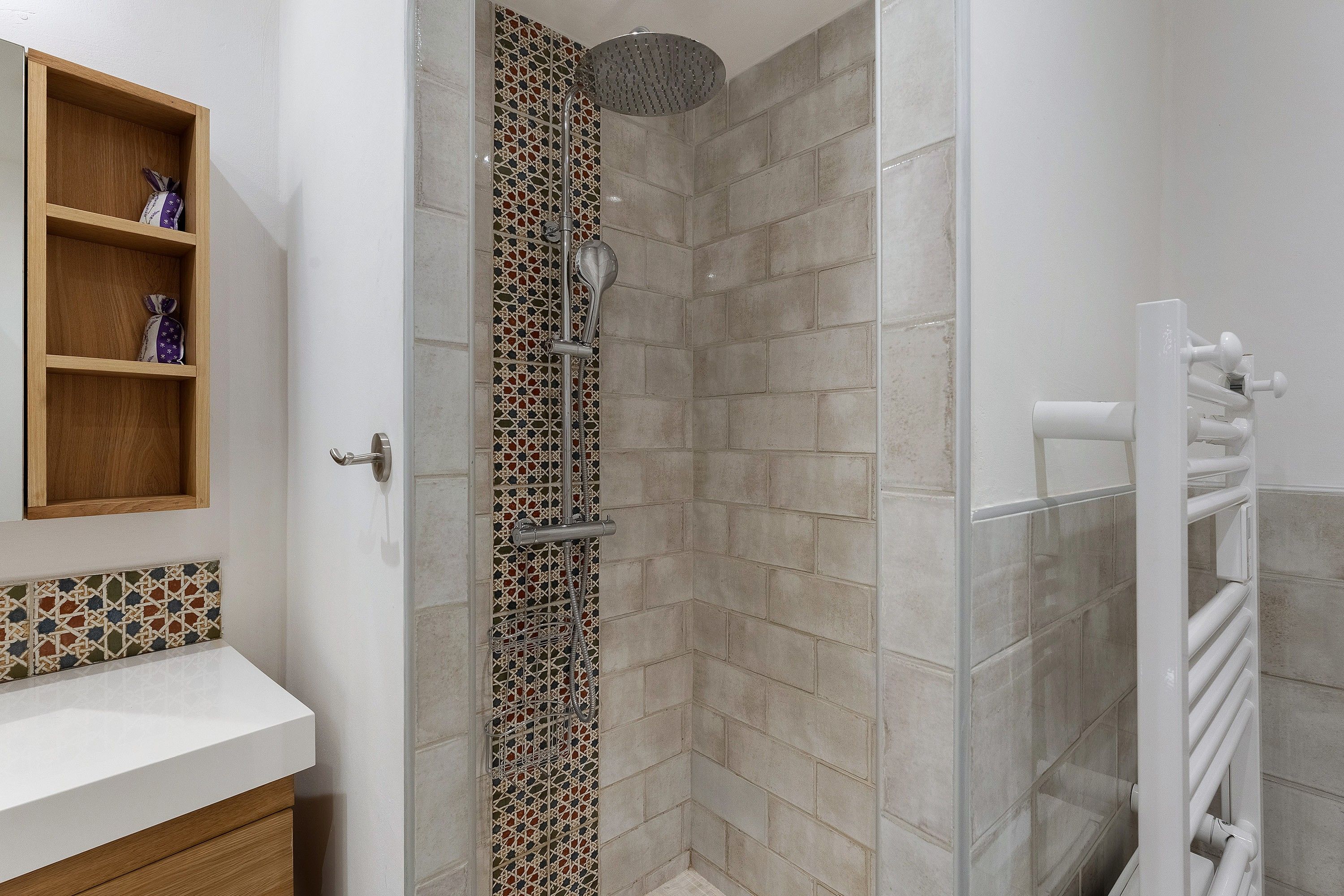 Une salle de bain avec une douche, une étagère en bois ornée d’objets décoratifs et un lavabo blanc.