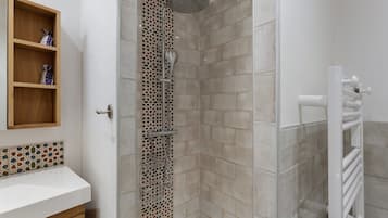Une salle de bain avec une douche, une étagère en bois ornée d’objets décoratifs et un lavabo blanc.