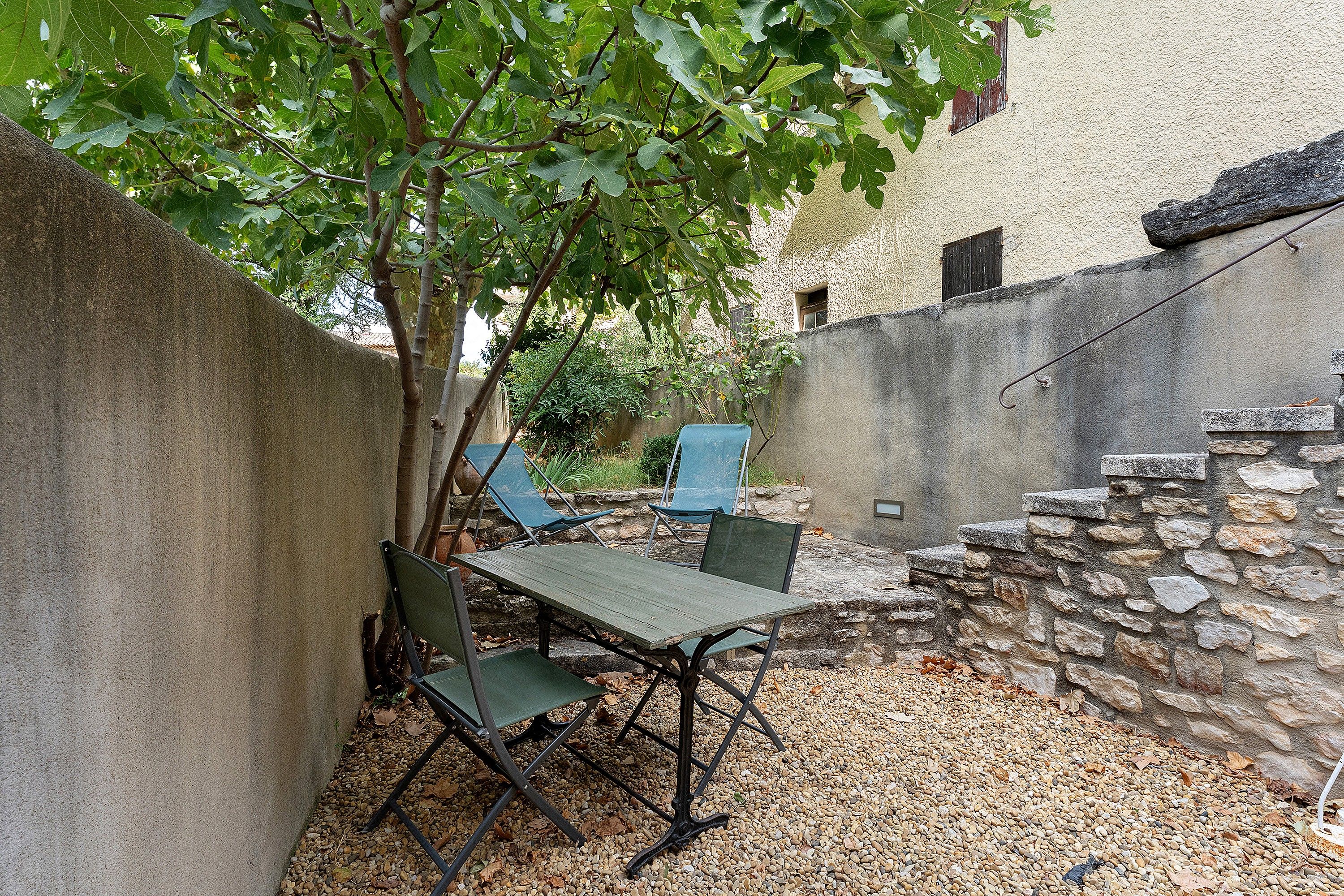 A courtyard with a table and chairs, surrounded by a stone wall and a tree.