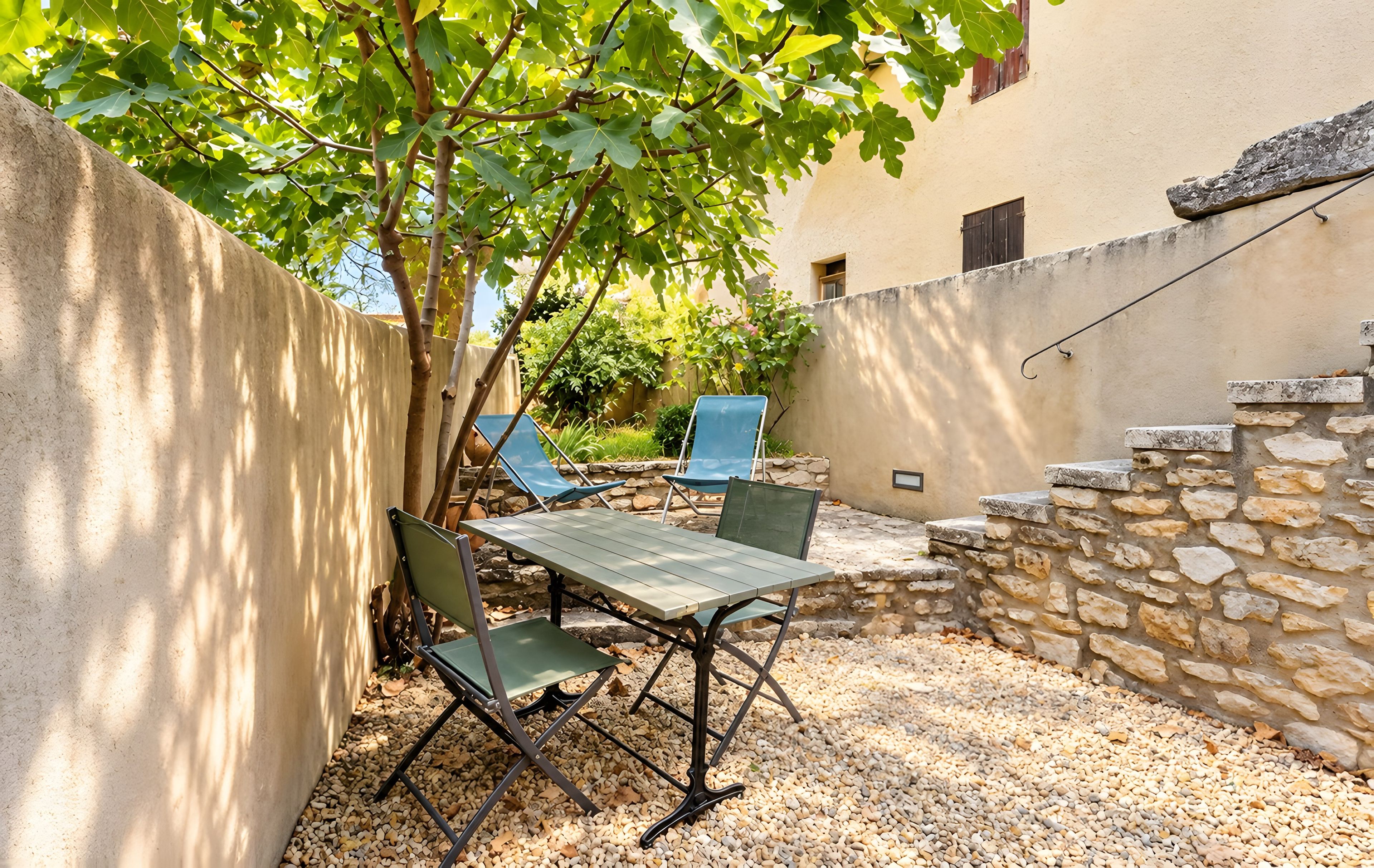 Un patio con una mesa y sillas, rodeado por un muro de piedra y un árbol.