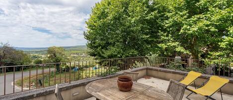 A balcony with a table and chairs, a potted plant, and a view of the countryside.