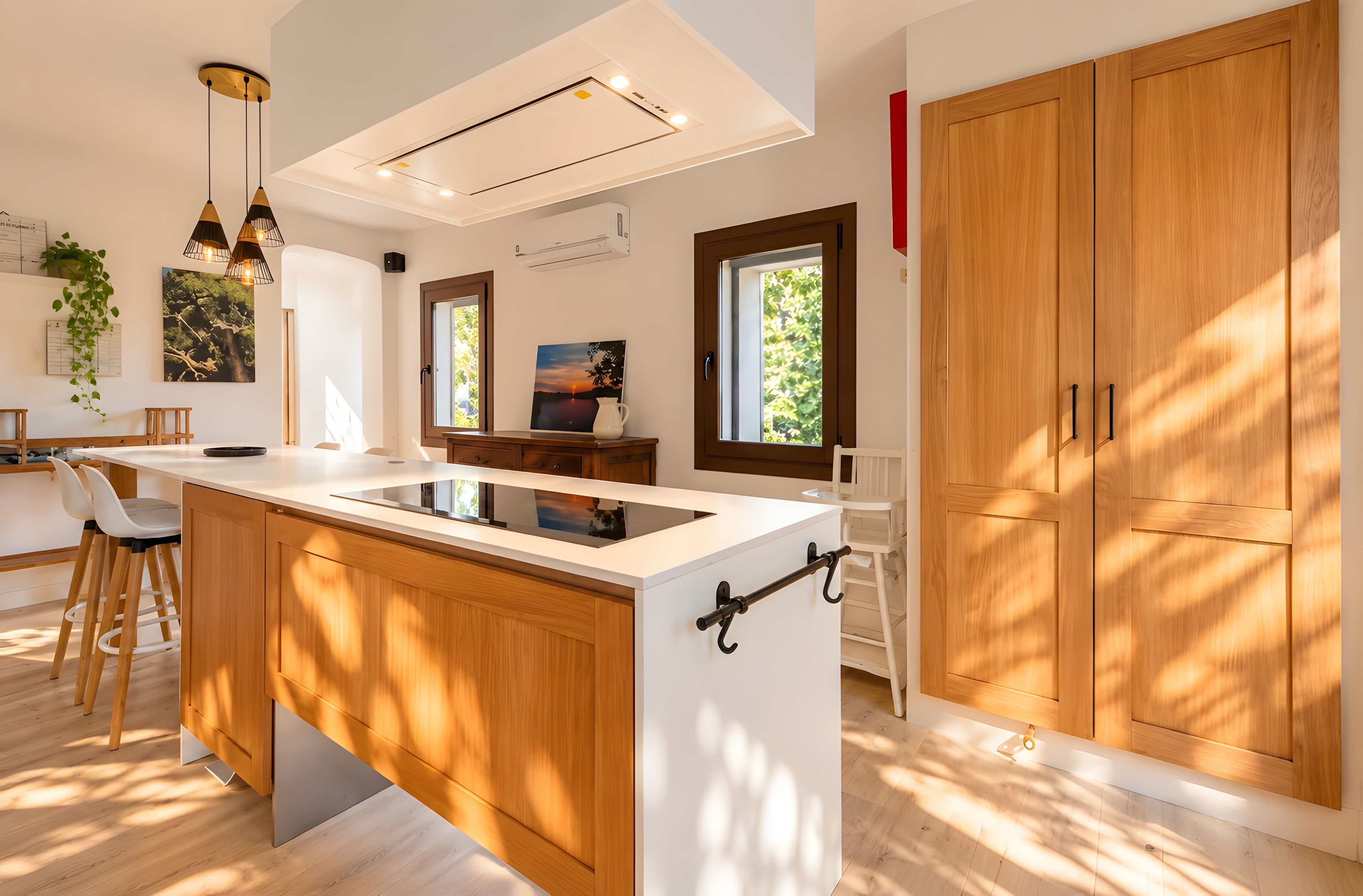 A modern kitchen with a central island, wooden cabinets, pendant lighting, and a view of greenery outside.